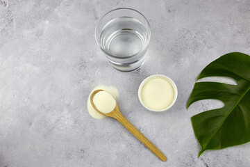 Collagen protein powder  and a glass of water on grey background. Natural beauty and health supplement for skin, bones, joints.