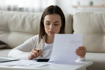 Head shot focused young lady holding banking mortgage payment notification, managing household budget alone at home. Serious woman calculating incomes outcomes earnings expenditures indoors.