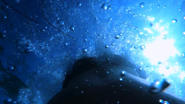 Man diving in the ocean as seen from the back of a person. Descending in the deep sea. Air bubbles ascending while exhaling. First person view, slow motion