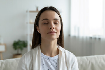 Peaceful young beautiful woman breathing fresh air, enjoying mindful woman alone at home, head shot. Mindful pretty millennial girl doing yoga breathing exercises with closed eyes, inspiration moment.
