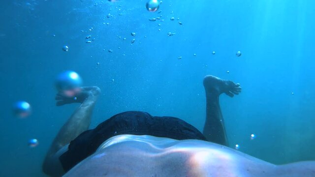 Man diving in the ocean as seen from the back of a person. Descending in the deep sea. Air bubbles ascending while exhaling. First person view, slow motion