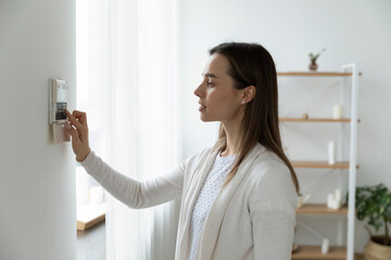 Fototapeta na wymiar Side view pleasant young woman using smart home system or activating modern alarm system before leaving apartment. Happy lady turning off easy security technology, when returning house or flat.