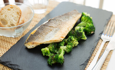 fried fillet of sea bass with garnish of broccoli on black warm stone plate