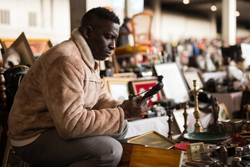 Obraz premium ordinary Afro-American guy considers things sacond hands on flea market