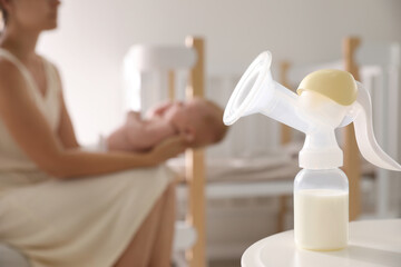 Mother and little baby indoors, focus on table with breast pump