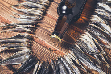 Small dry fish on a rope on a wooden background and brown beer bottle