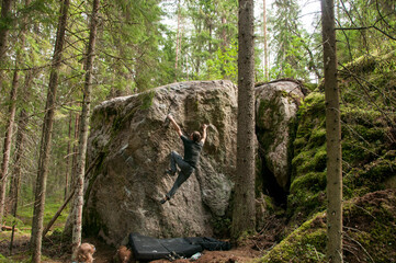 Man climbing a bouldering problem on a rock covered with green moss. Bouldering in a magic wood....