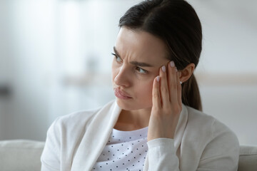 Head shot close up frustrated unhealthy woman touching temples, suffering from strong migraine or severe headache indoors. Stressed millennial girl thinking of hard difficult decision alone at home.