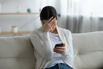 Stressed young woman holding telephone, feeling confused of bad news notification. Unhappy...