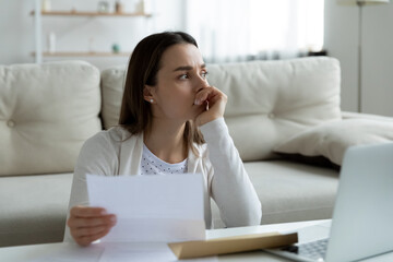 Thoughtful unhappy frustrated young woman holding paper letter with banking termination...