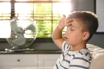 Little boy suffering from heat near fan at home. Summer season © New Africa