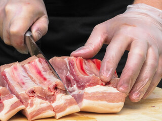 Obraz na płótnie Canvas a man cuts meat into steaks. gloved hand. meat pork on the bone