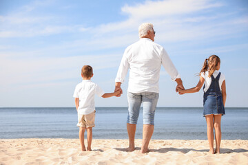 Cute little children with grandfather spending time together on sea beach, back view