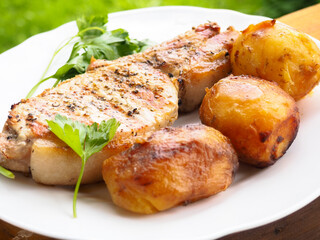 roast pork steak on a plate with potatoes and herbs. rosemary.