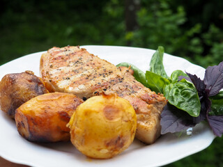roast pork steak on a plate with potatoes and herbs. rosemary.