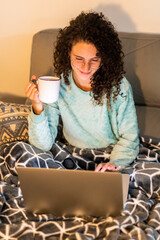 Stock photo of a young woman with glasses curly hair at home using macbook laptop relaxing on the...