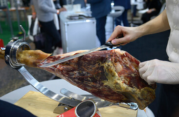 Barman hands cutting off slice pieces of smoked meat from a gammon using knife