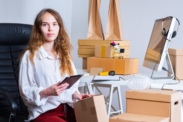 An employee of an online store looks at the camera. The girl is preparing orders for shipment....