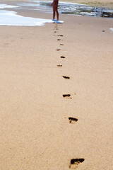 feet of a young girl walk barefoot on a wet beach, leaving footprints in the sand