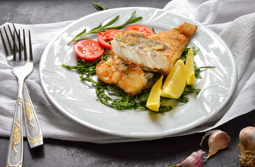 Fried fish fillet with tomatoes, lemon and rosemary. White plate. Dark background. White linen napkin.