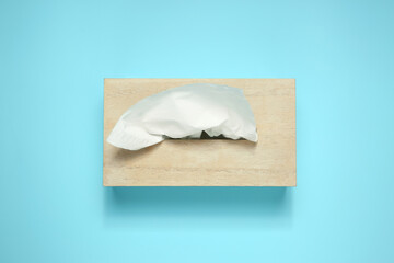 Wooden holder with paper tissues on light blue background, top view