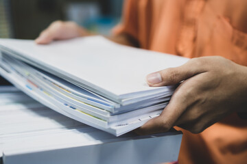 Office workers employee holding stacks of lot documents report papers waiting be managed on desk in busy office. Workload in businessman finacial paperwork information unfinished document achieves