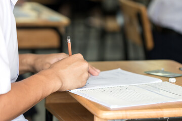 Student taking school exam of educational admission test in class and writing answer paper in...