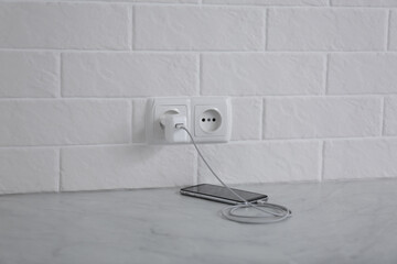 Modern mobile phone with charger near white brick wall on floor