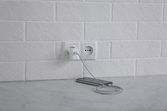 Modern Mobile Phone With Charger Near White Brick Wall On Floor