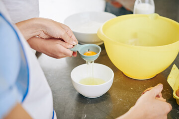 Close-up image of mother showing daughter how to use plastic tool for separating egg white and yolk