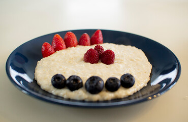 Oatmeal porridge with berries, in a blue plate. Healthy breakfast.