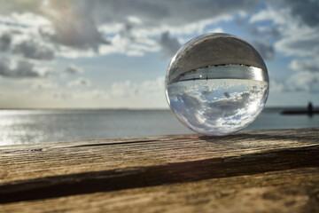 View through a crystal ball on an old extended wooden bench over the sea with the mudflats and the sky with clouds