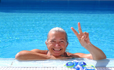 Senior happy woman smiles at the poolside making ok gesture with her hand enjoying the day of...