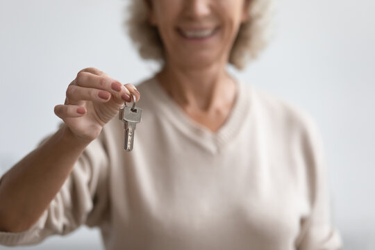 Close up smiling mature woman holding house keys, satisfied middle aged female customer buying dwelling, apartment, making successful real estate deal, purchasing property, elderly mortgage program