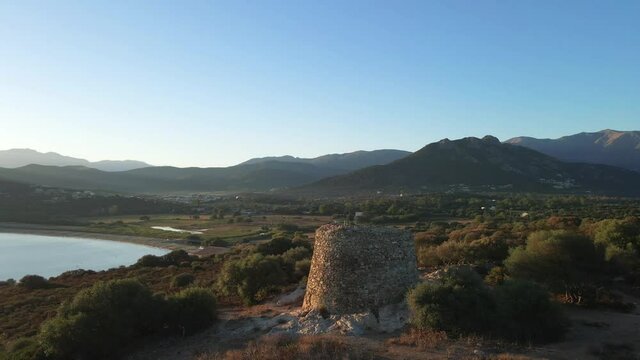 Aerial view zooming out from the ancient Genoese tower at Losari in corsica with the beach and mountains in the background