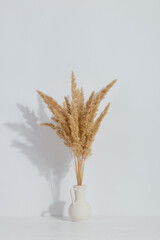 A vase with yellow spikelets on the table, on a white background. Light stylish design.