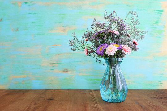 bouquet of colorful field flowers in the glass blue vase over wooden table