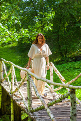 Naklejka na ściany i meble A beautiful woman in a white dress walks along a birch bridge