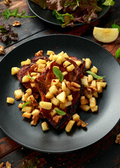 Roasted Pork chops with caramelized apples, walnuts and sage in black plate on wooden table