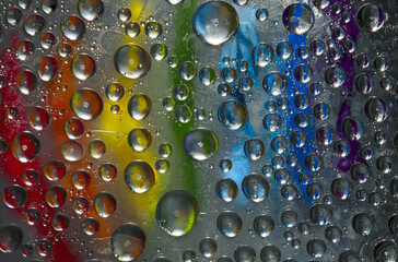 Rounded ice particles are located on the mirror ice surface against the background covered with rainbow-colored paints. Abstract fantasy.