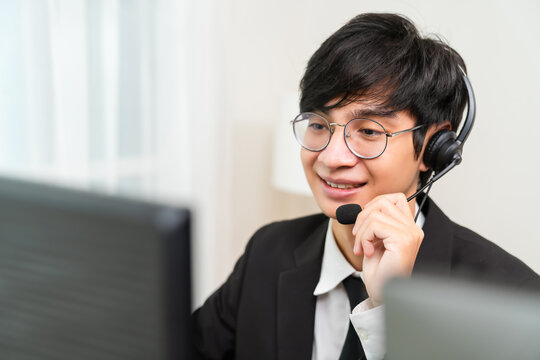 Smiling Asian businessman consultant wearing a microphone headset of customer support phone operator at the workplace.