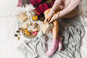 Cozy soft  image of  young woman  in warm woolen clothes is sitting on her bed  in  bright  sunny...