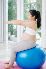 Fototapeta na wymiar Pregnant Asian woman doing exercise on fitness ball at home in the morning