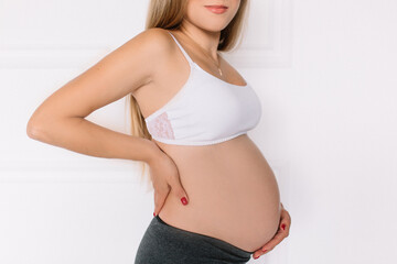
A pregnant woman stands in a bra and holds her belly