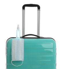 Stylish turquoise suitcase, antiseptic spray and protective mask on white background. Travelling during coronavirus pandemic