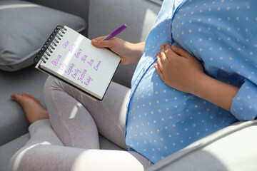 Pregnant woman with baby names list sitting on sofa, closeup - obrazy, fototapety, plakaty