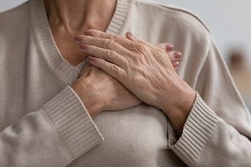 Close up cropped image hopeful grateful mature senior woman keeping hands on chest, mindful middle...