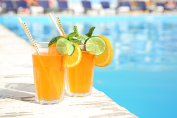 Refreshing cocktail in glasses near outdoor swimming pool on sunny day
