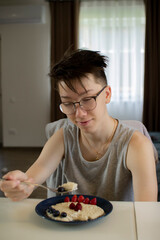 A teenager eats oatmeal porridge with berries.
