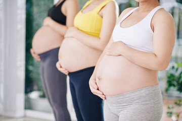 Pregnant women in sports bras and leggings touching bellies and getting ready for yoga class